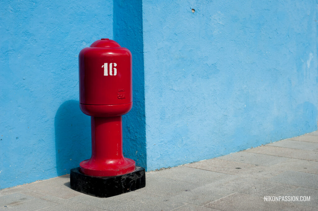 Cadrage et composition en photo : Une borne incendie rouge sur fond bleu, le contraste de couleur attire le regard vers la borne