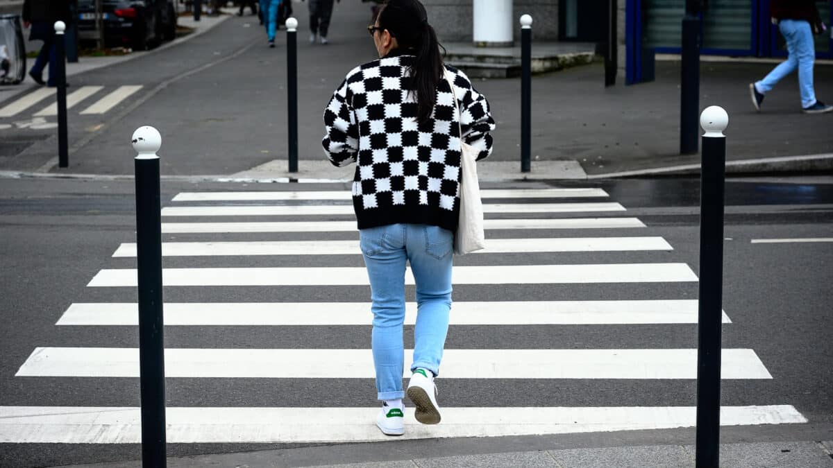 Une femme avec une veste à carreaux noir et blanc traverse un passage piéton à bandes noires et blanches - illustration de "Droit à l’image pour les photographes : que pouvez-vous photographier et publier ?"
