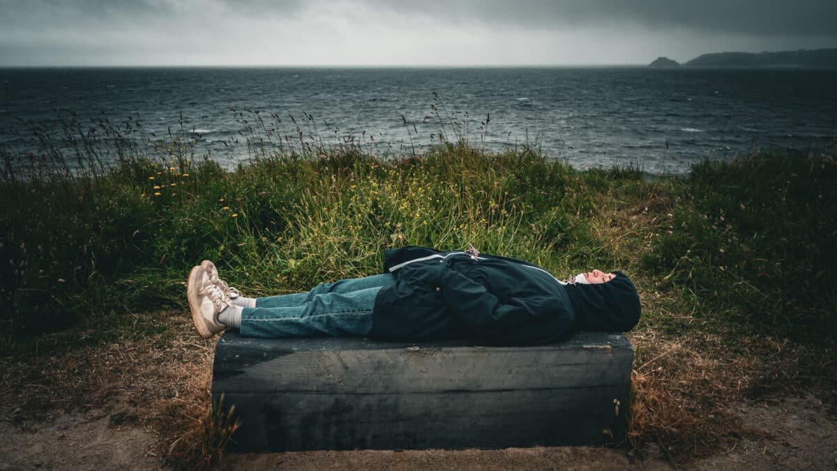 Jeune femme couchée sur un banc face à un paysage de bord de mer en Bretagne