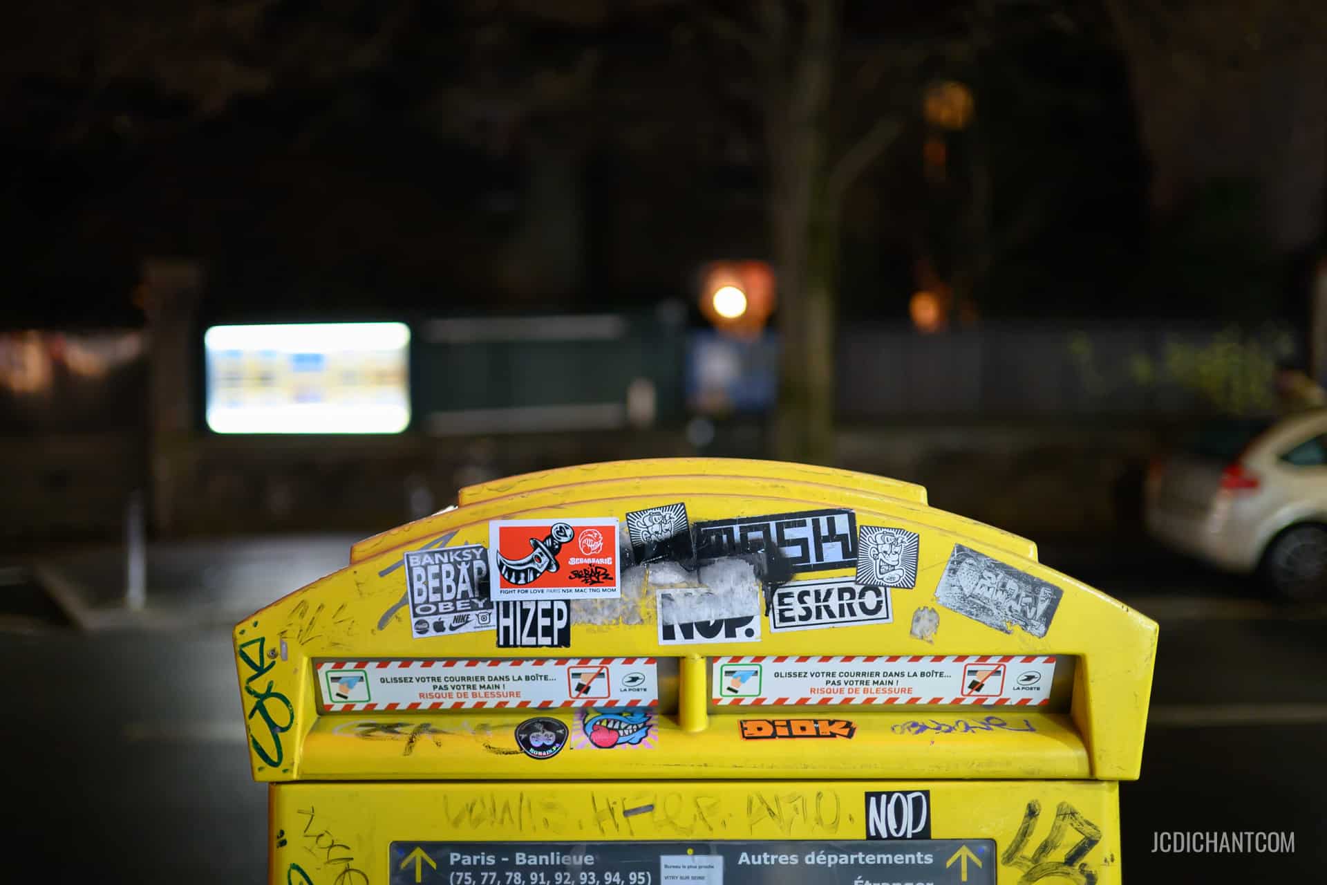 Boîte à lettres jaune dans la rue de nuit avec des stickers colorés - photo (©) JC Dichant